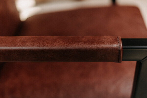 Vue détaillée de l'accoudoir en cuir marron avec coutures apparentes sur la chaise cantilever de salle à manger.